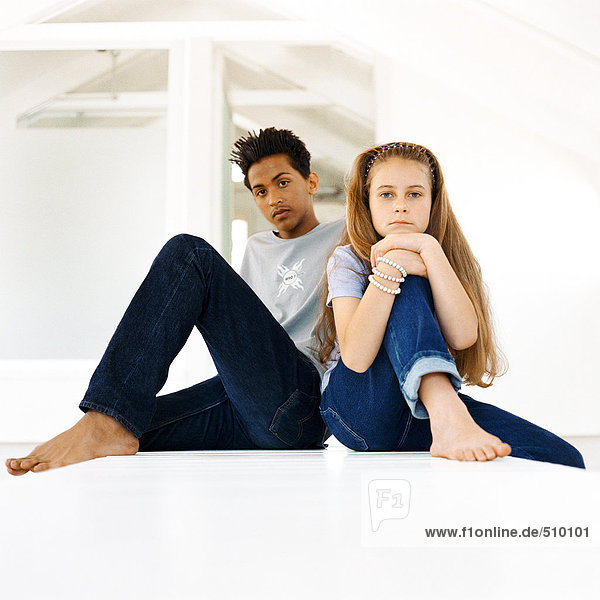Teenage boy and girl sitting with knees up  looking into camera  portrait