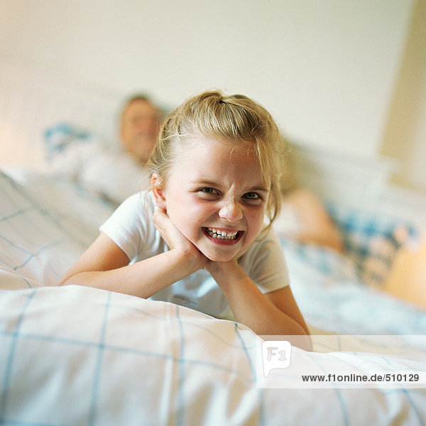 Girl lying at end of parent's bed  making face