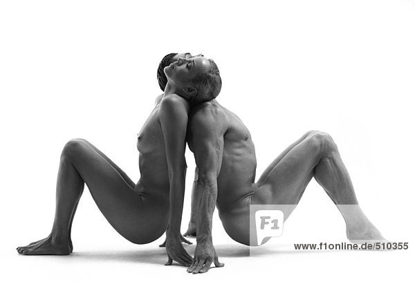 Nackter Mann und Frau Rücken an Rücken in sitzender Position mit hochgezogenen Knien  Balancieren auf Füßen und Fingern  s/w