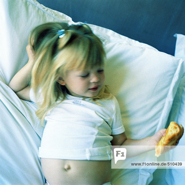 Kind auf dem Bett liegend  Croissant haltend