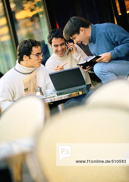 Drei Männer sitzen auf der Café-Terrasse mit Laptop-Computer
