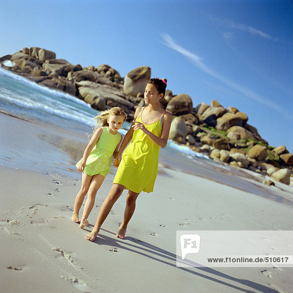 Mädchen und kleine Schwester halten sich an den Händen  während sie am Strand spazieren gehen.
