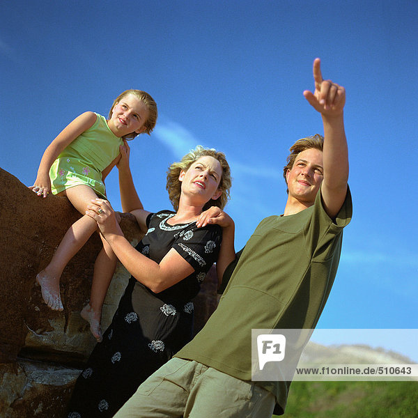 Teen boy pointing  standing next to mother and little sister