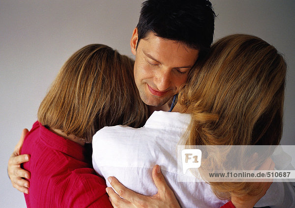 Mann umarmt zwei Frauen  Augen geschlossen