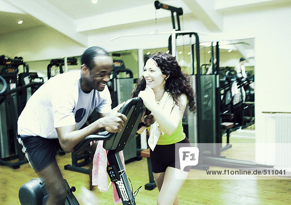 Frau steht neben dem Mann mit Trainingsgeräten im Fitnessstudio  lacht