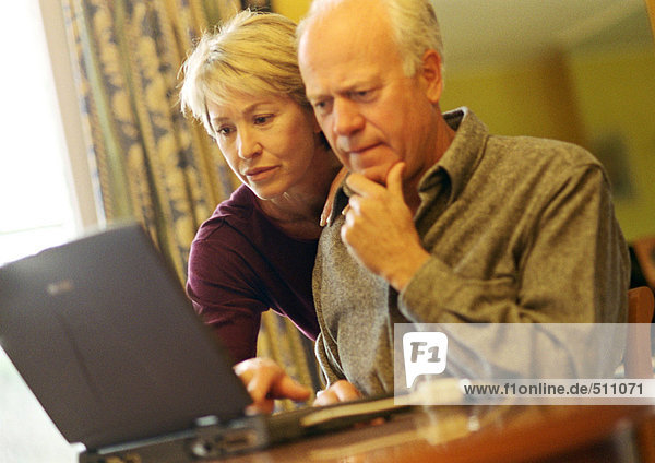 Mature couple  man using laptop  woman looking over shoulder