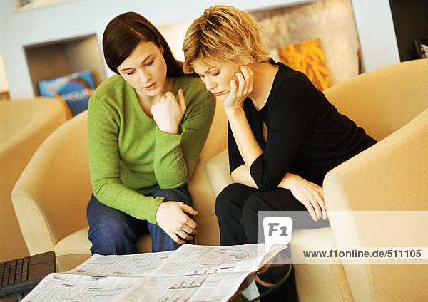 Zwei Frauen sitzend  Zeitung lesend