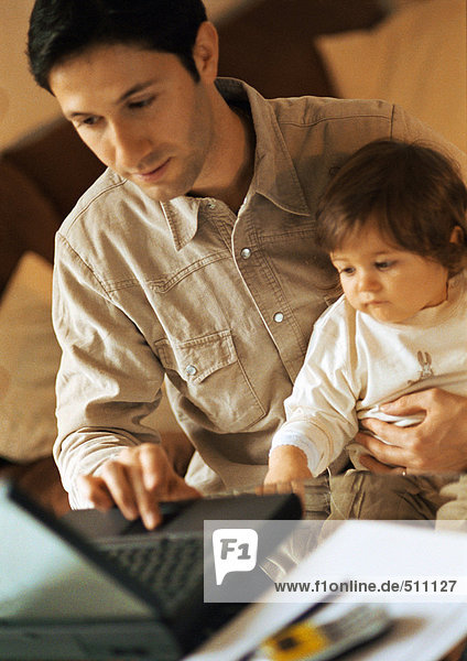 Father and baby  father using laptop  baby sitting on father's lap.