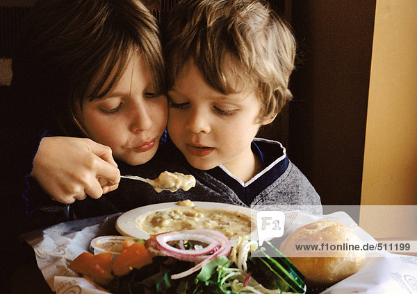 Kleiner Junge hilft dem jüngeren Bruder beim Essen  Porträt.
