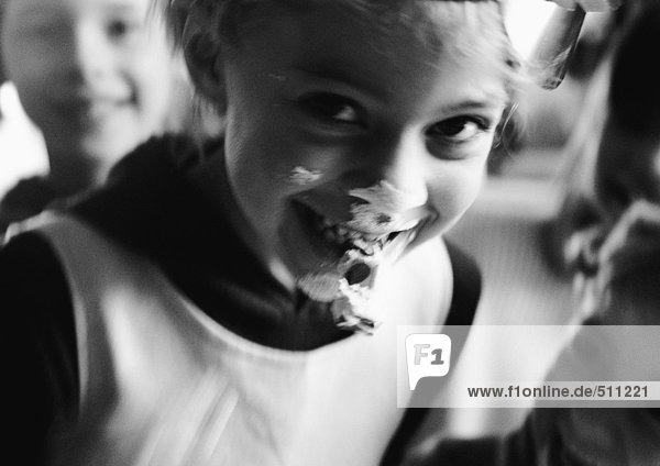 Junges Mädchen lacht mit Essen im Gesicht  schaut in die Kamera  mit anderen Kindern  s/w.