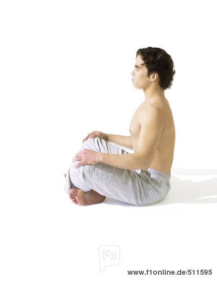 Oben-ohne-Mann auf dem Boden sitzend  meditierend  Seitenansicht