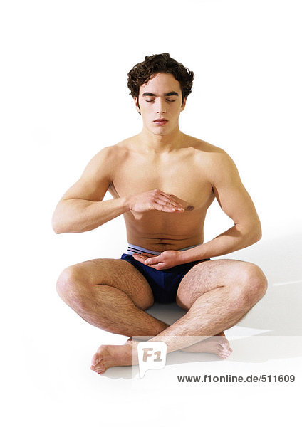 Man in underwear sitting indian style on floor with hands hovering