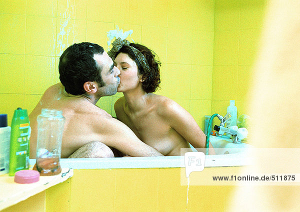 Paar in der Badewanne sitzend,  küssend,  Seitenansicht.