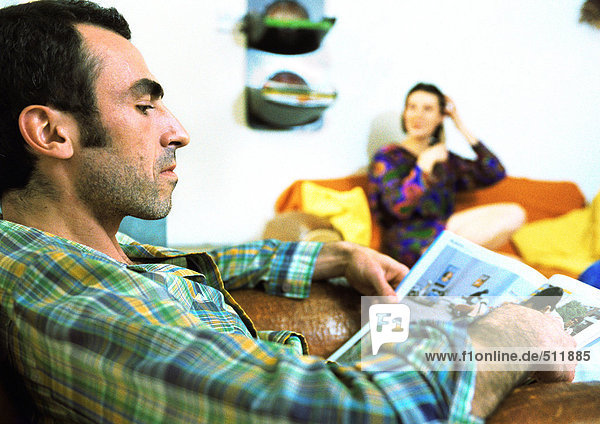 Mann liest Magazin  Frau sitzt im Hintergrund.
