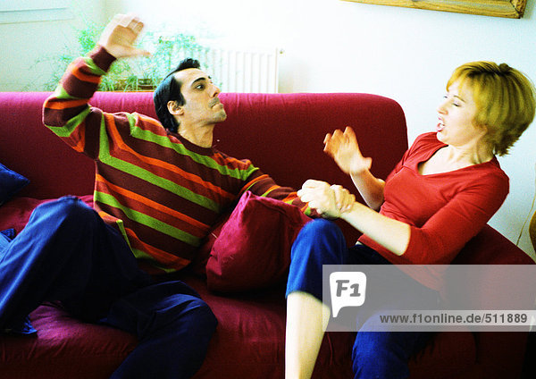 Ein Paar auf dem Sofa kämpfend,  die Hand des Mannes erhoben,  die Frau zuckend.