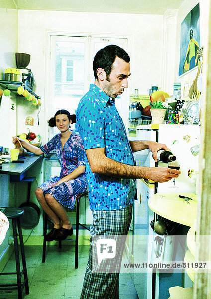 Paar in der Küche  Frau sitzt  Mann gießt Wein.