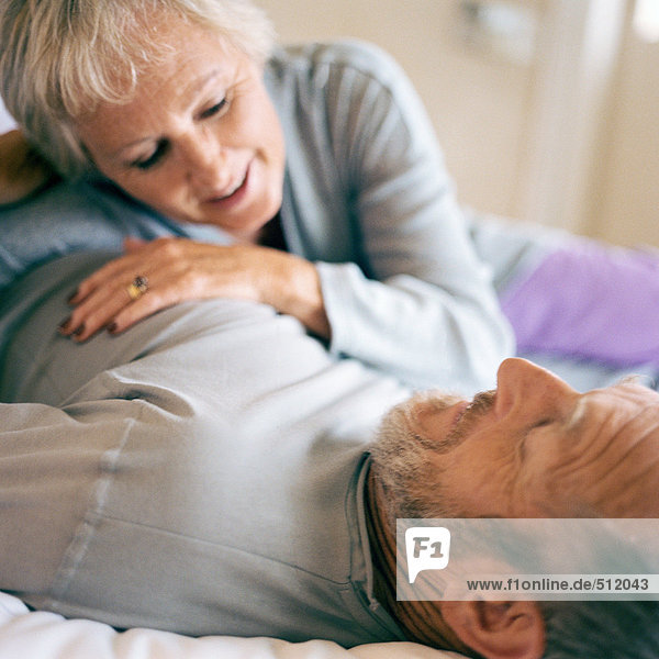 Seniorenpaar liegend  Frau auf dem Bauch des Mannes lehnend