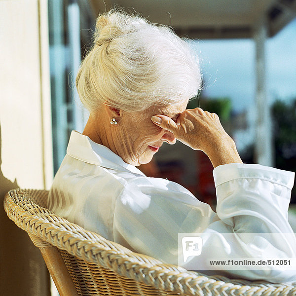 Seniorin in der Sonne sitzend mit Hand über den Augen  Seitenansicht