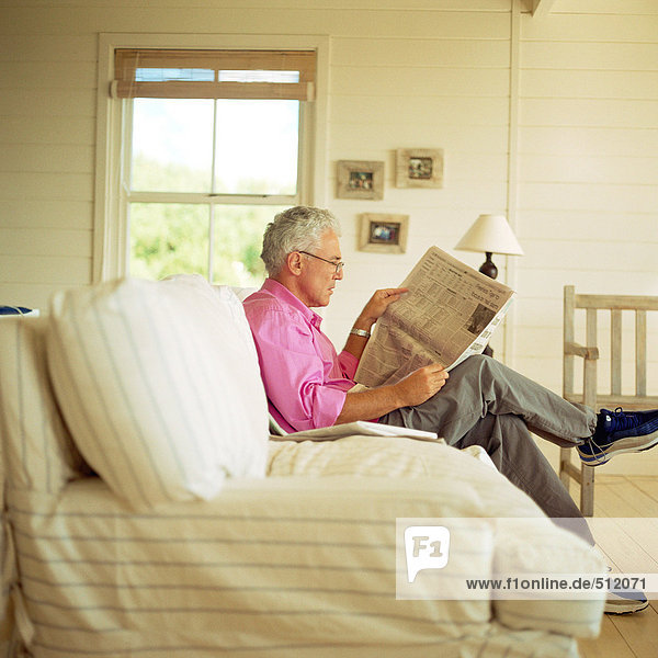 Mature man sitting on sofa  reading newspaper  side view