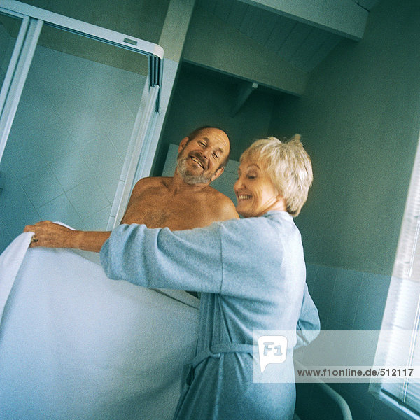 Reife Frau hält Handtuch vor nacktem Mann