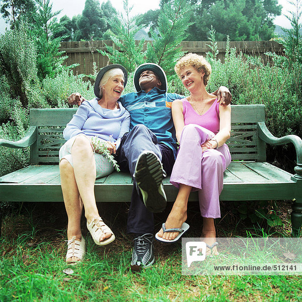 Ein reifer Mann sitzt zwischen zwei Frauen auf einer Bank.