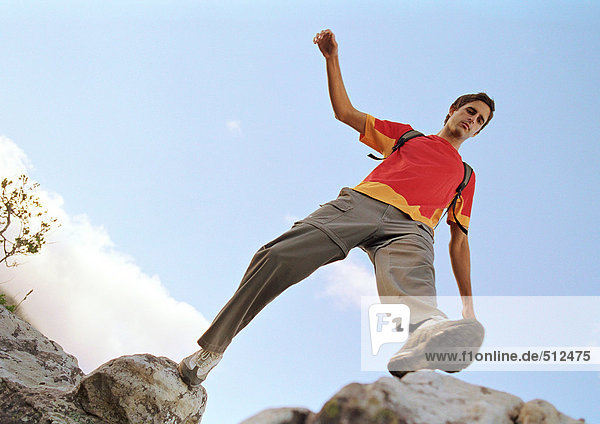 Young man stepping across rocks  low angle view.