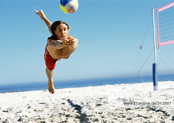 Junger Mann springt zum Volleyball  in der Luft.