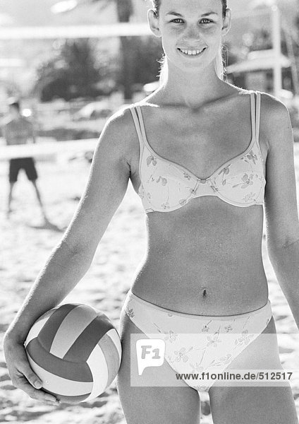 Junge Frau lächelt am Strand  hält Volleyball  Porträt  s/w.
