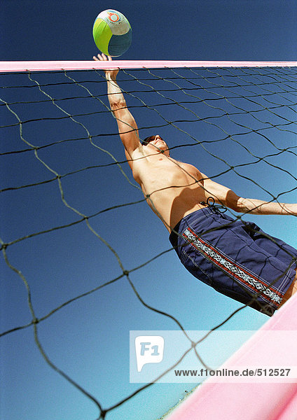 Junger Mann spielt Beachvolleyball  schlägt Ball über Netz  Blickwinkel niedrig.