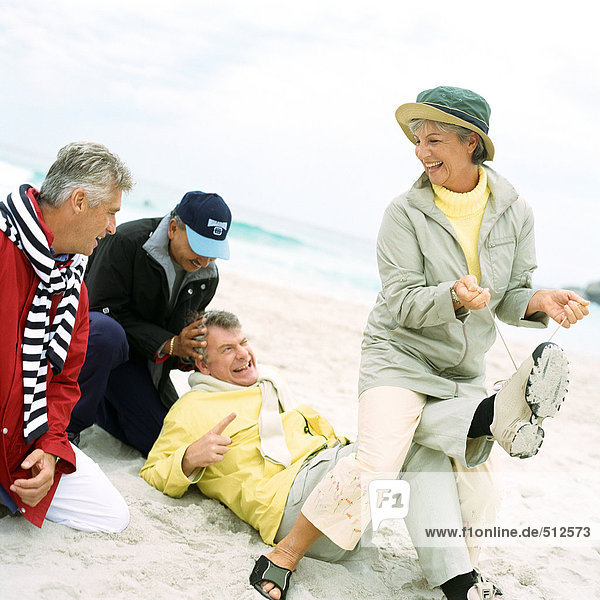Mature group playing on beach  woman pulling man's laces