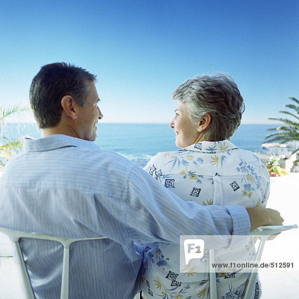 Erwachsenes Paar am Strand sitzend  Männerarm um Frau  Rückansicht