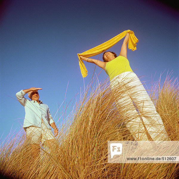 Mature couple standing in tall grass  woman holding scarf above head