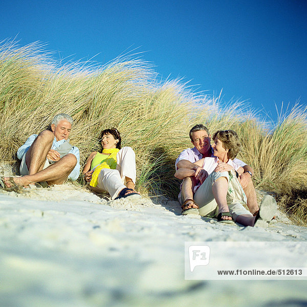 Two mature couples sitting on beach