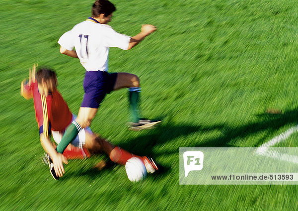 Fußballspieler greift nach dem Ball  Gegner springt über das Bein  verschwommen.