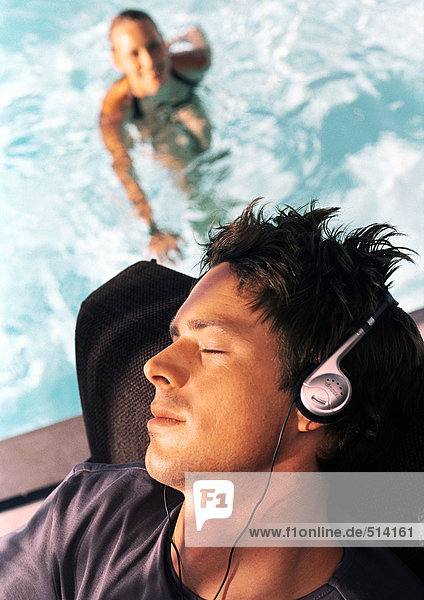 Mann mit Kopfhörer  Frau im Schwimmbad im Hintergrund  Weitwinkelansicht