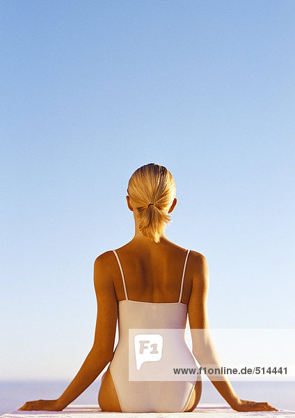 Frau im einteiligen Badeanzug  Hände zur Seite  Taille hoch  Rückansicht  blauer Himmel im Hintergrund