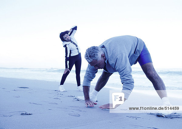 Mature man and woman stretching on beach