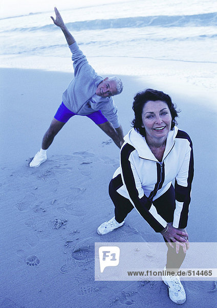 Mature man and woman stretching on beach