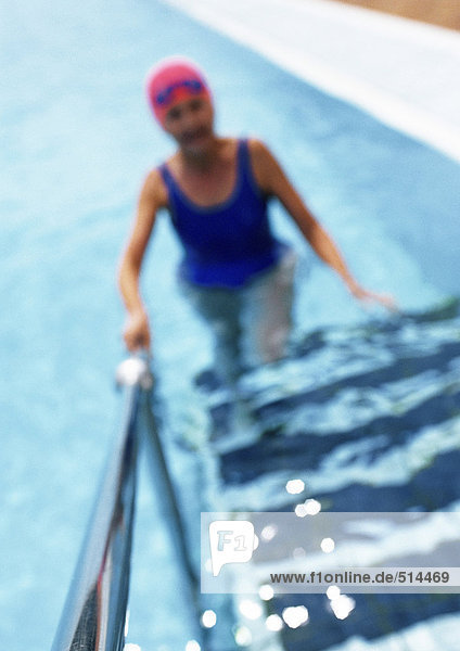 Mature woman in swimming pool  walking up ladder  blurred
