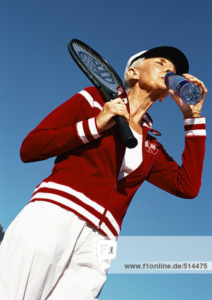 Reife Frau hält Tennisschläger und trinkt aus der Wasserflasche  Blickwinkel niedrig