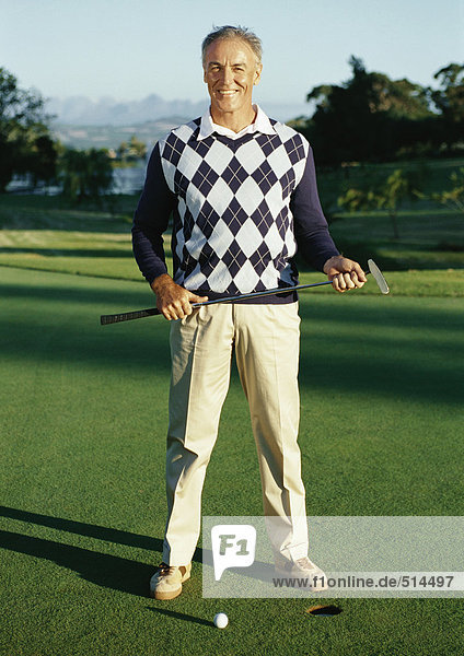 Mature man holding golf club next to hole  portrait