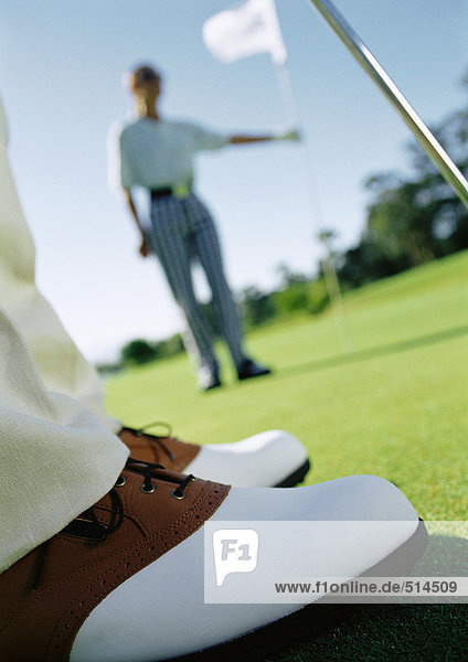Golfer's feet on green  and second golfer holding pole