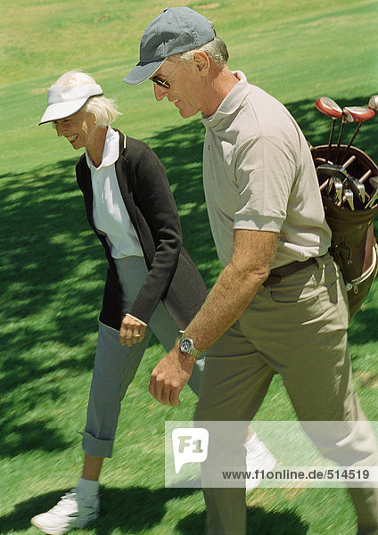 Mature man and woman on green  man carrying golf clubs