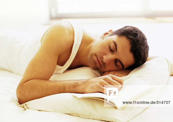 Mann im Bett liegend mit Hand auf Buch und geschlossenen Augen