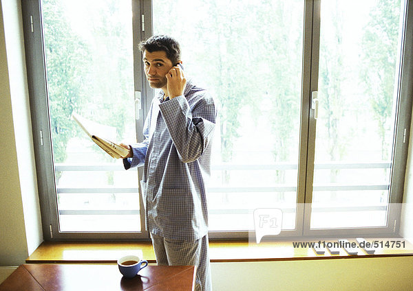 Mann im Pyjama mit Handy und Zeitung lesen