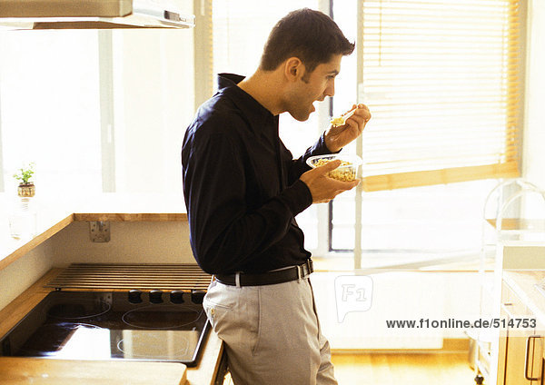 Mann beim Essen im Stehen in der Küche