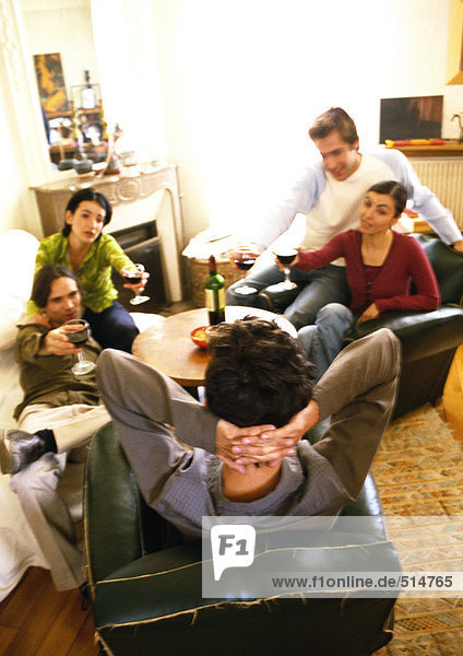 Junge Leute sitzen im Wohnzimmer und trinken Wein.