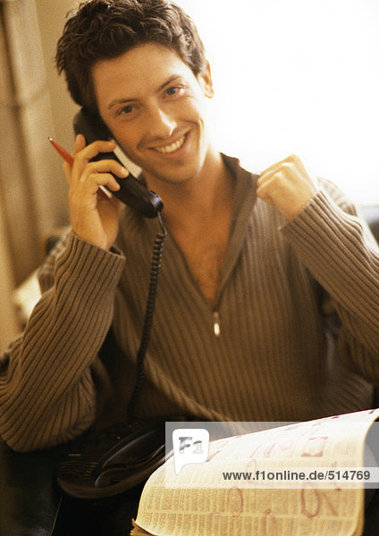 Mann telefoniert mit Zeitung auf Knien,  lächelnd