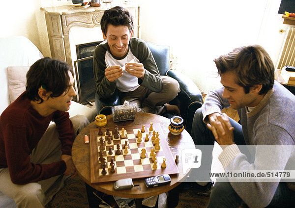 Drei Männer im Wohnzimmer  zwei spielen Schach.