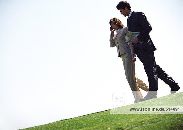 Geschäftsmann und Frau mit Handy  auf Gras gehend